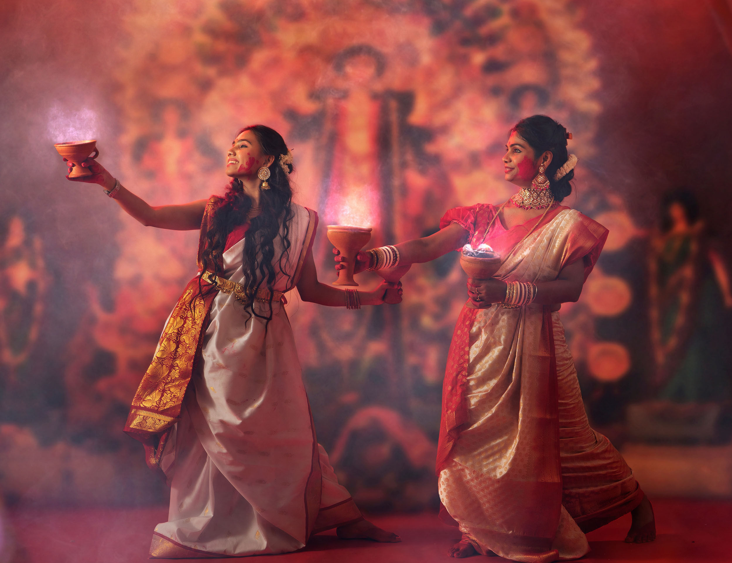 Two women performing 'Dhunuchi Naach' (Dhunuchi Dance) with earthen lamps, a vibrant ritual during Durga Puja celebrations.
